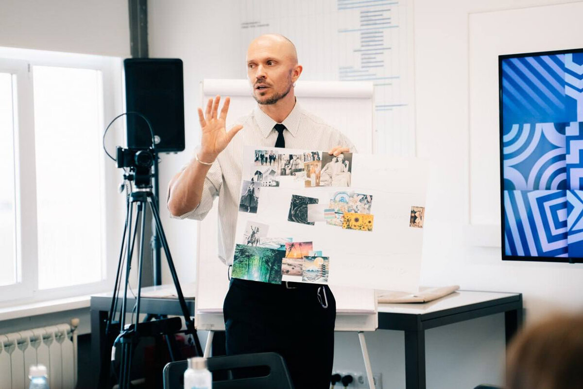 Anton Kopylov holding up a printed moodboard collage while teaching a class