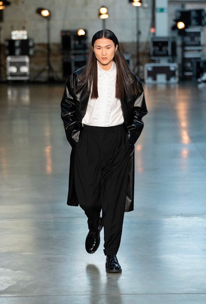 Runway look: long black leather coat over a ruffled white shirt and drop-crotch trousers