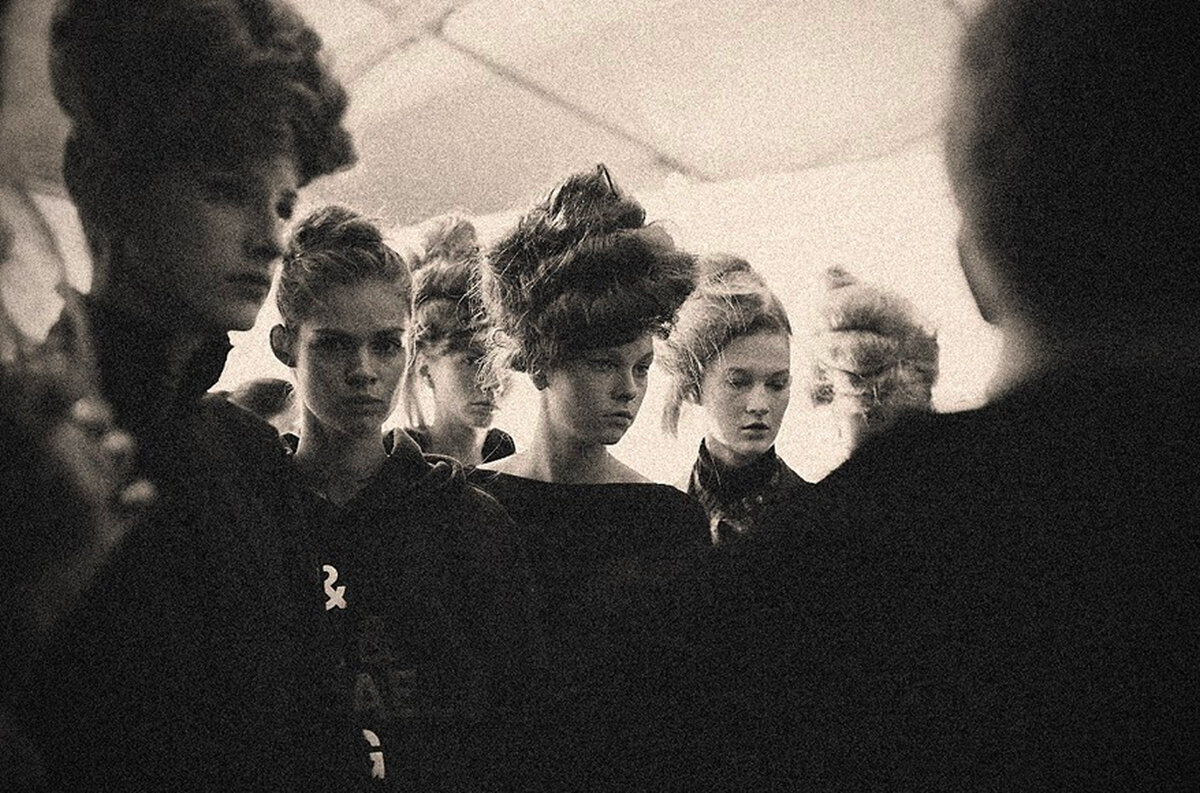 Grainy backstage shot of models in teased updos waiting in line before a show