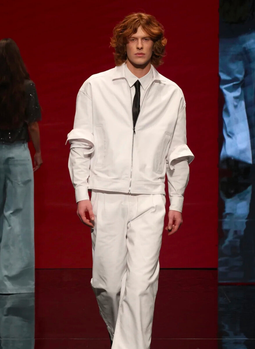 Runway look: white zip jacket and trousers with a black tie, against a red backdrop