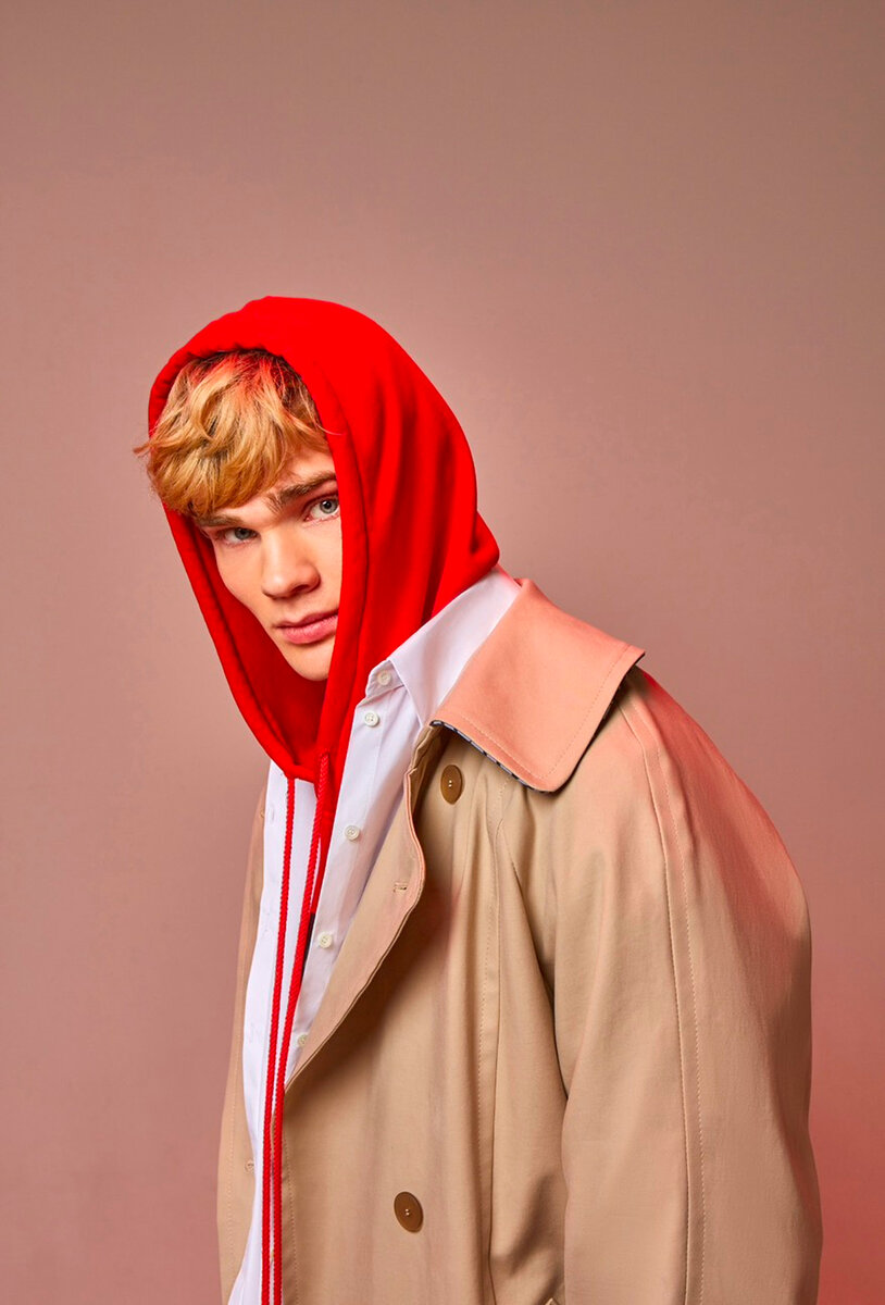 Male model in beige double-breasted trench over a white shirt and red hood