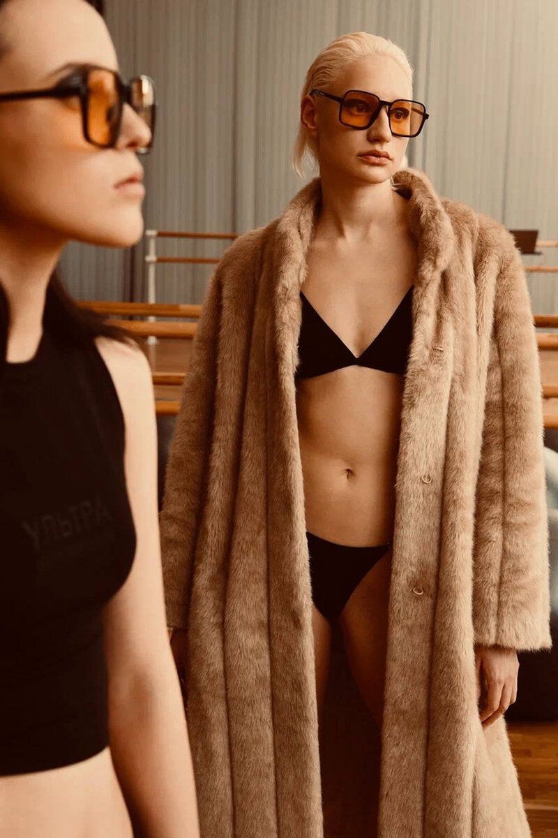 Models wearing beige faux-fur coat over black swimwear, and a black tank top and tinted glasses